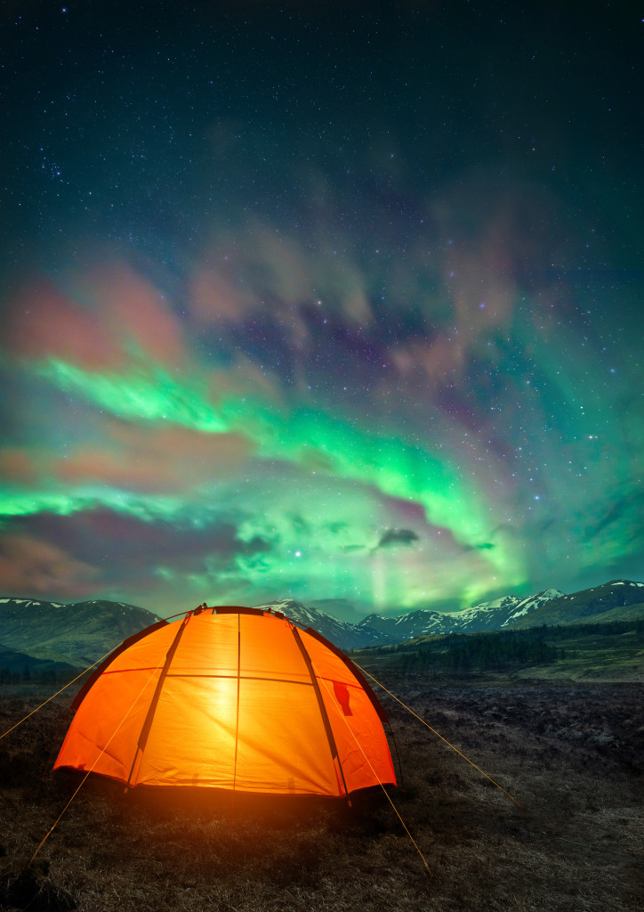 A camping tent glowing under the Northern Lights. Night time camping scene.